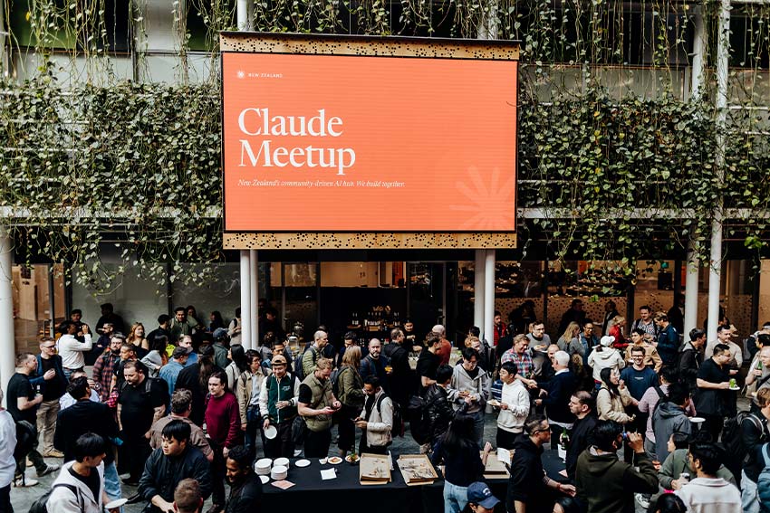 A large banner announces the currently running Claude Meetup above the heads of attendees