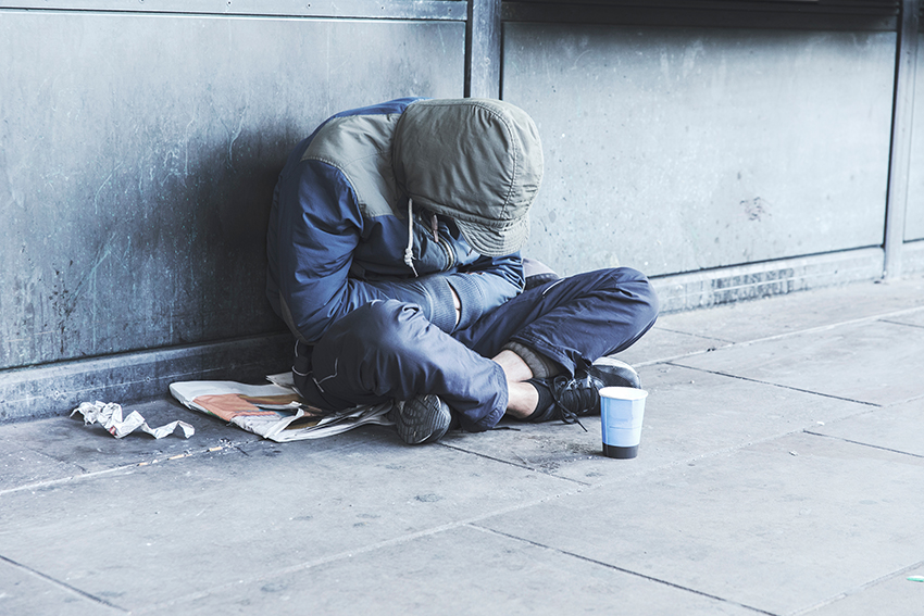 A homeless man sitting crossed legs with a cup in front.