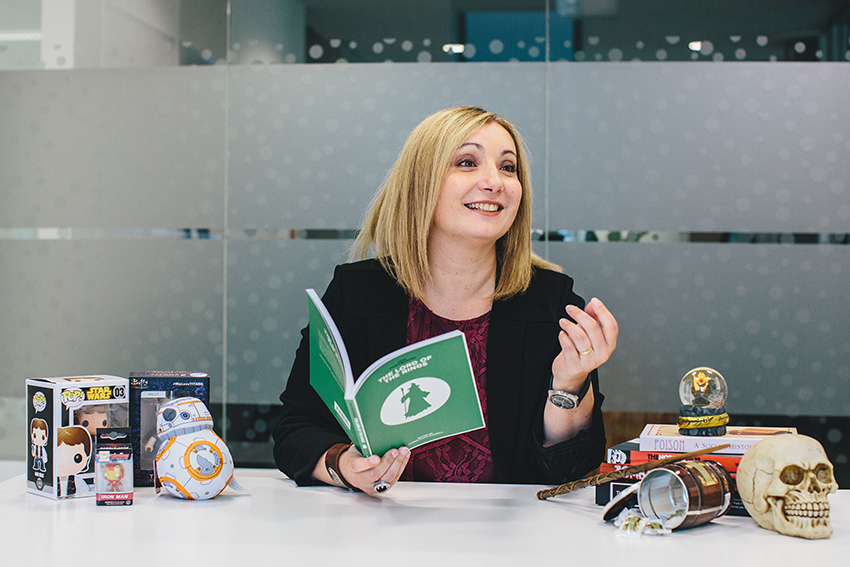 Professor Lorna Piatti-Farnell sitting at a desk and holding a book.