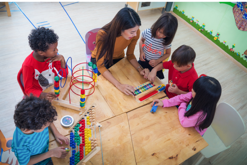 Early childhood education teacher teaching five young children at a low desk.