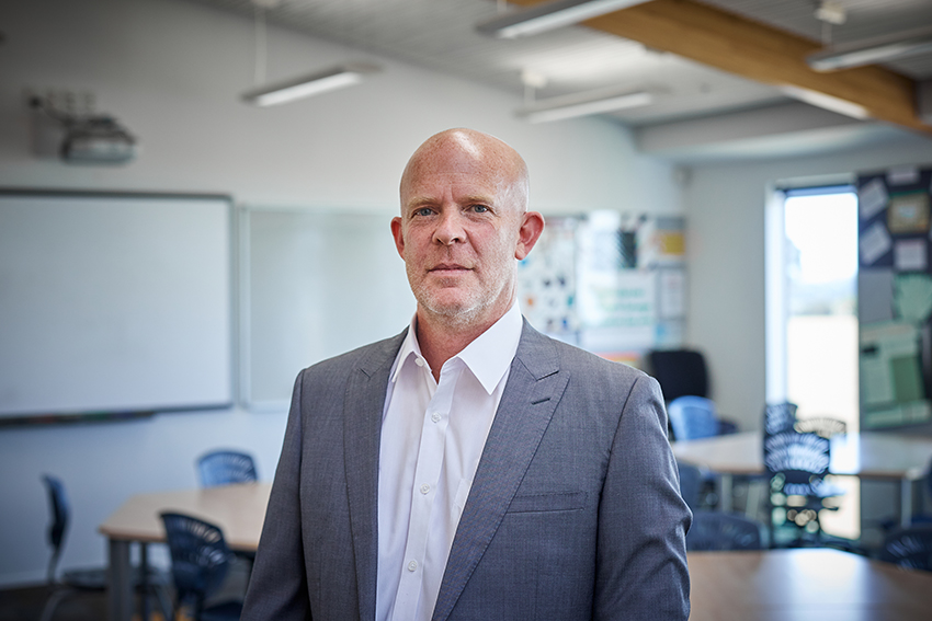 Associate Professor Andrew Gibbons standing in a classroom.