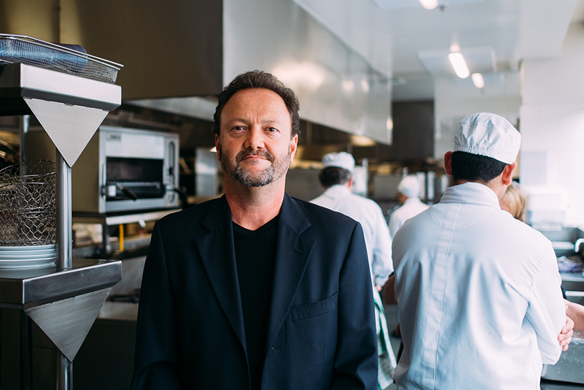 Dr David Williamson standing in a commercial kitchens with chefs busy making food behind him.