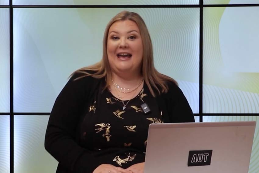 A person sitting at a desk with a laptop, looking at the camera and ready to talk