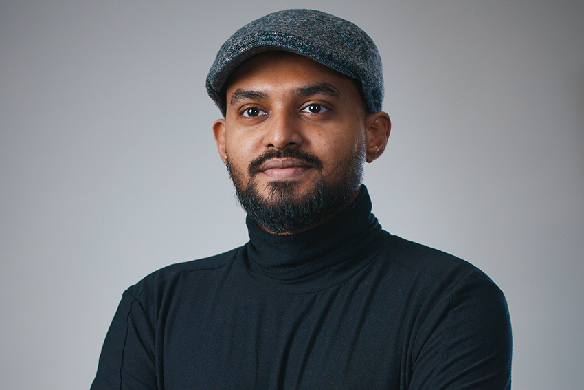 A head and shoulders shot of a man in grey hat, black beard and black polo top.
