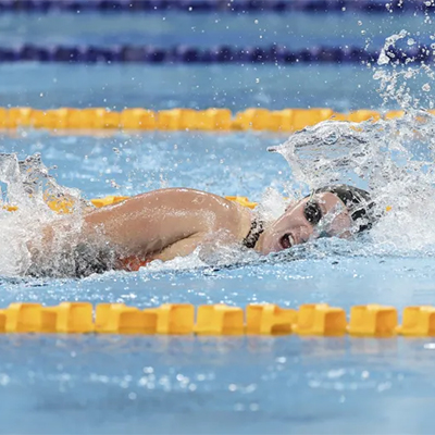 Swimmer turns to breathe mid-stroke during a freestyle race, with water splashing between the lane ropes.