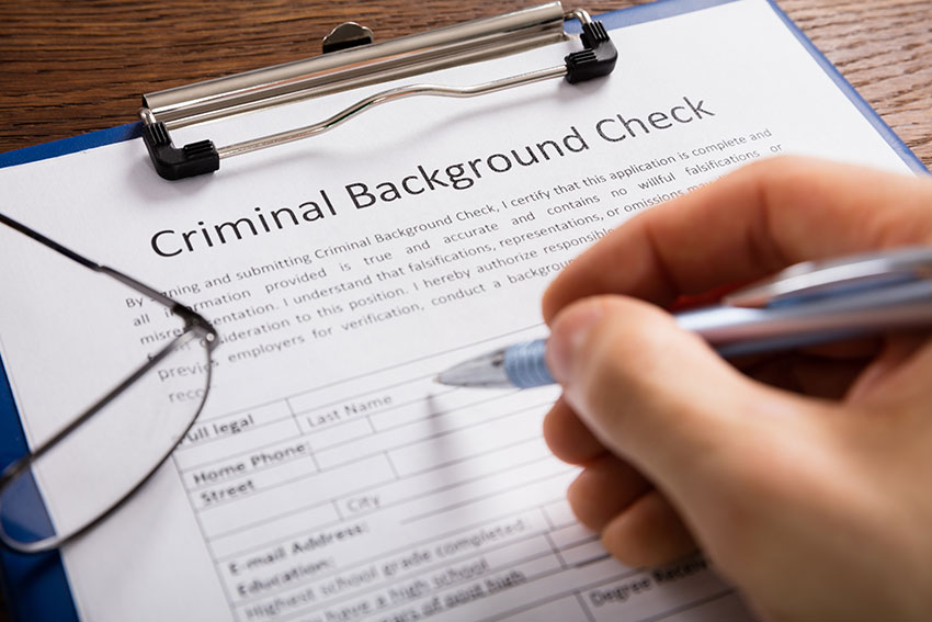 Close-up Of Person Hand Filling Criminal Background Check Application Form