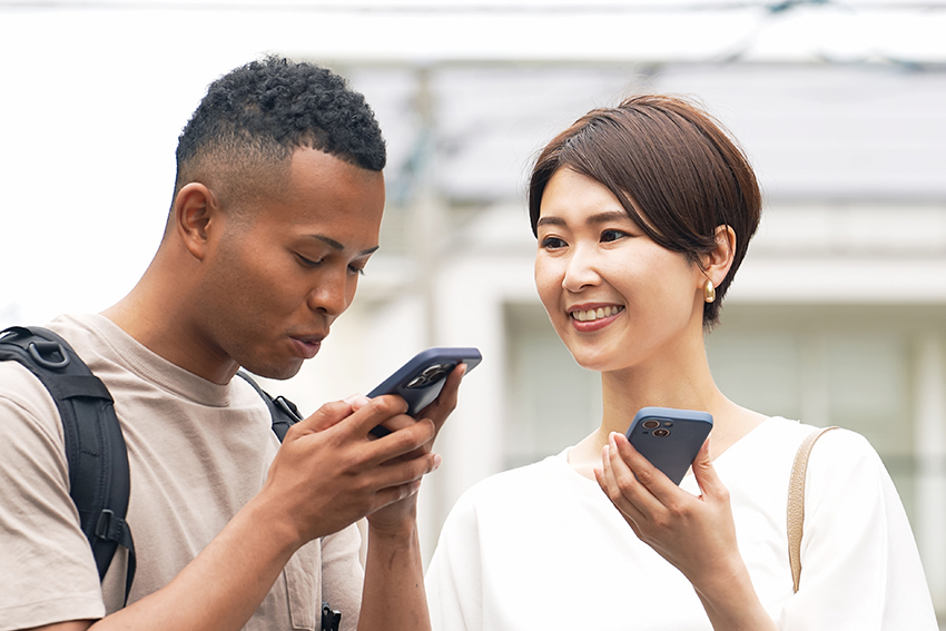 A black man and a Japanese woman usin a smartphone translation app to converse with each other.