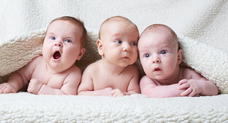 Three babies lying together on a blanket