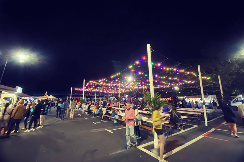 People enjoying the festival, with coloured strung up lights and bench seating.