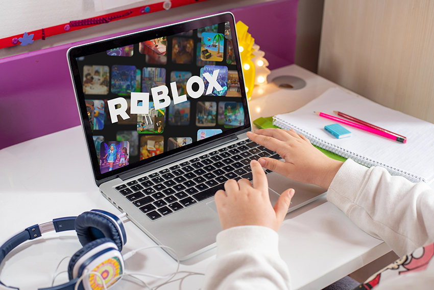 A child playing Roblox on a laptop. It is from the point of view of the child, with only their forearms visible.