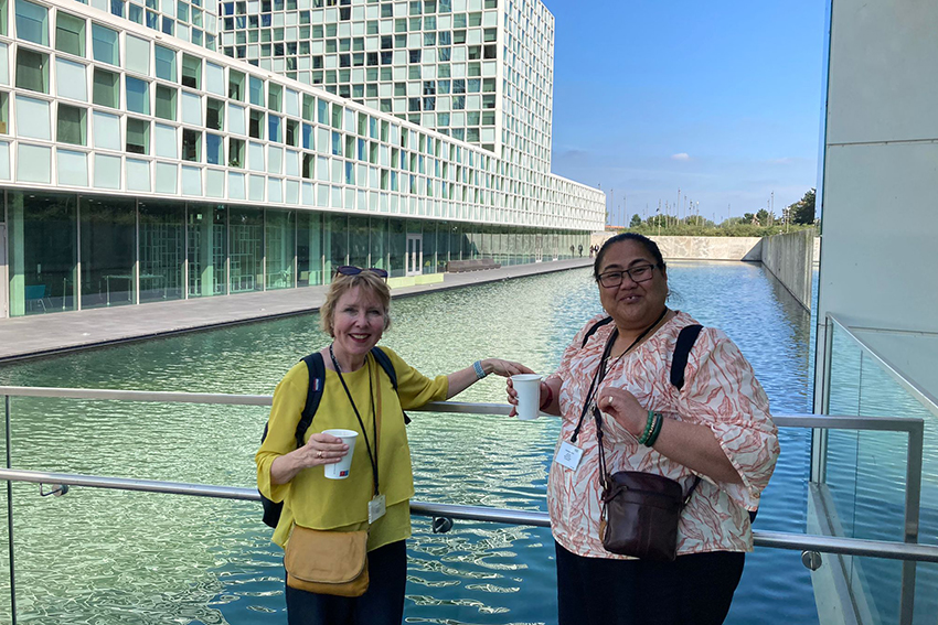 Two women standing in front of a large decorative pool with buildings behind.