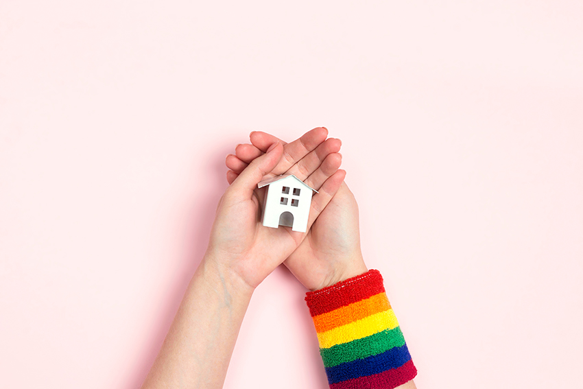 A young person's hands holding a small white house. There is a rainbow-coloured sweat band on their wrist.