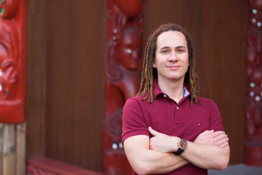 AUT Lecturer Hēmi Kelly standing arms crossed in front of the AUT marae.