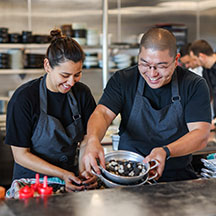 2 chefs in a kitchen helping each other