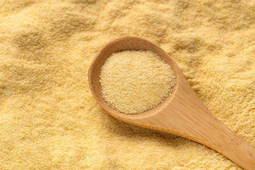 A stock image of durum wheat ground in a wooden spoon, with durum wheat ground behind.