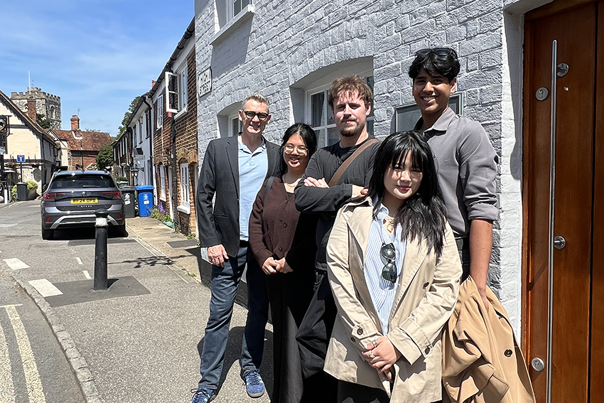The students and Geoff standing outside the grey brick building on an English street..