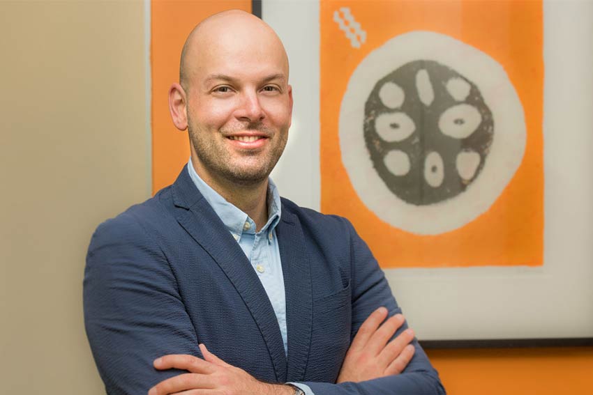 Matt Raskovic Man smiling with a painting in the background.