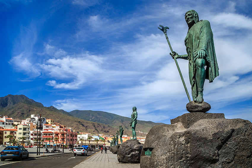 Bronze statues of guanche kings standing on boulders on the foreshore of the Canary Islands.