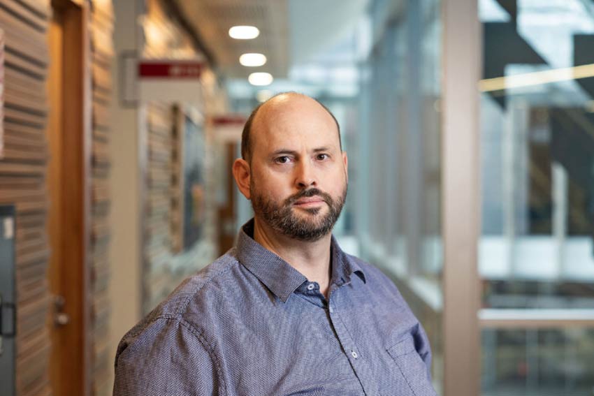 Aaron Gilbert photo 2 Man with a blank expression, standing in front the business school.