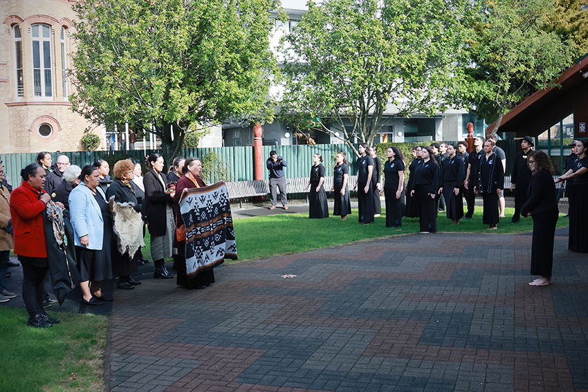 A photo out the front of AUT's wharenui showing Ngāti Whātua Ōrākei being welcomed on, holding the gifts.