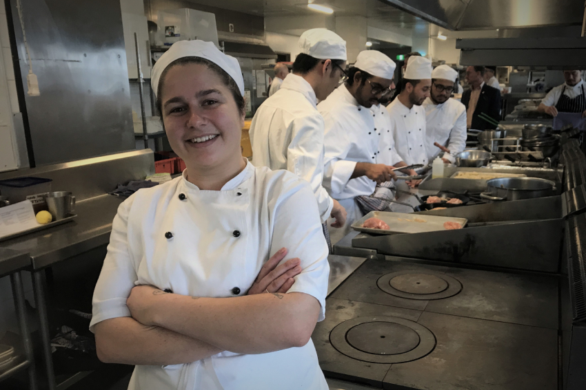 Hospitality student Sally Claire Nutt smiling in the foreground, with four of her fellow students preparing food behind.