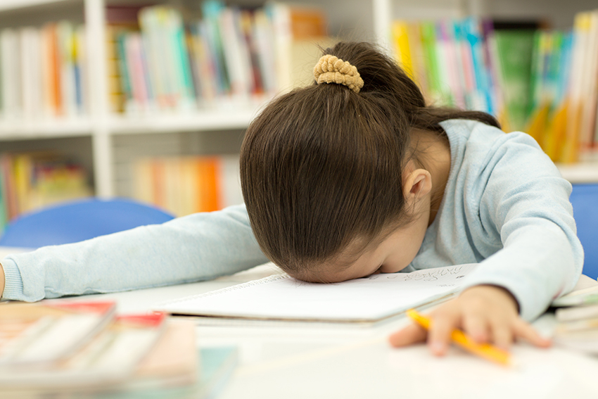 Young child face down on an exercise book at their school desk, disheartened.