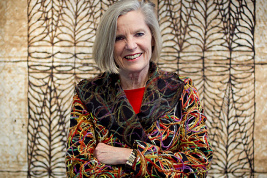 Professor Judy McGregor, smiling and standing in front of a Pacific Island artwork.