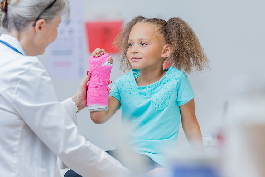 A health practitioner examines a child that has a cast on her arm.