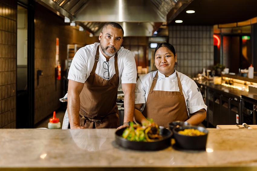 Gareth and Alisa stand behind their dish on the pass, wearing chef whites and brown aprons.